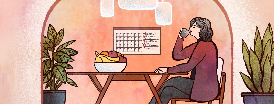 A woman sits at a table and sips calmly from a mug, her organized space helping her to feel calm.